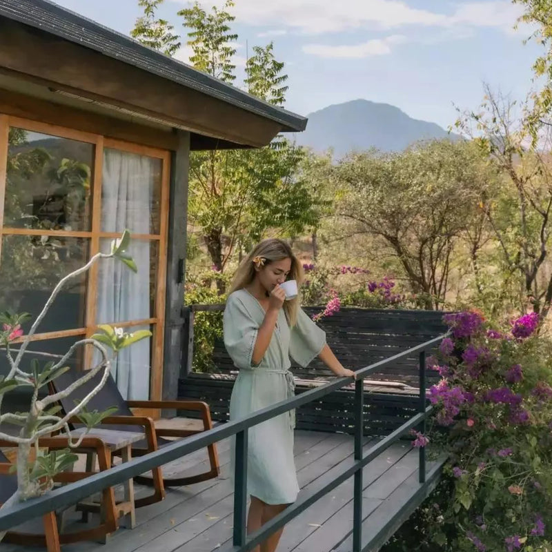 Woman in a green robe standing on a balcony with a scenic view of trees and mountains