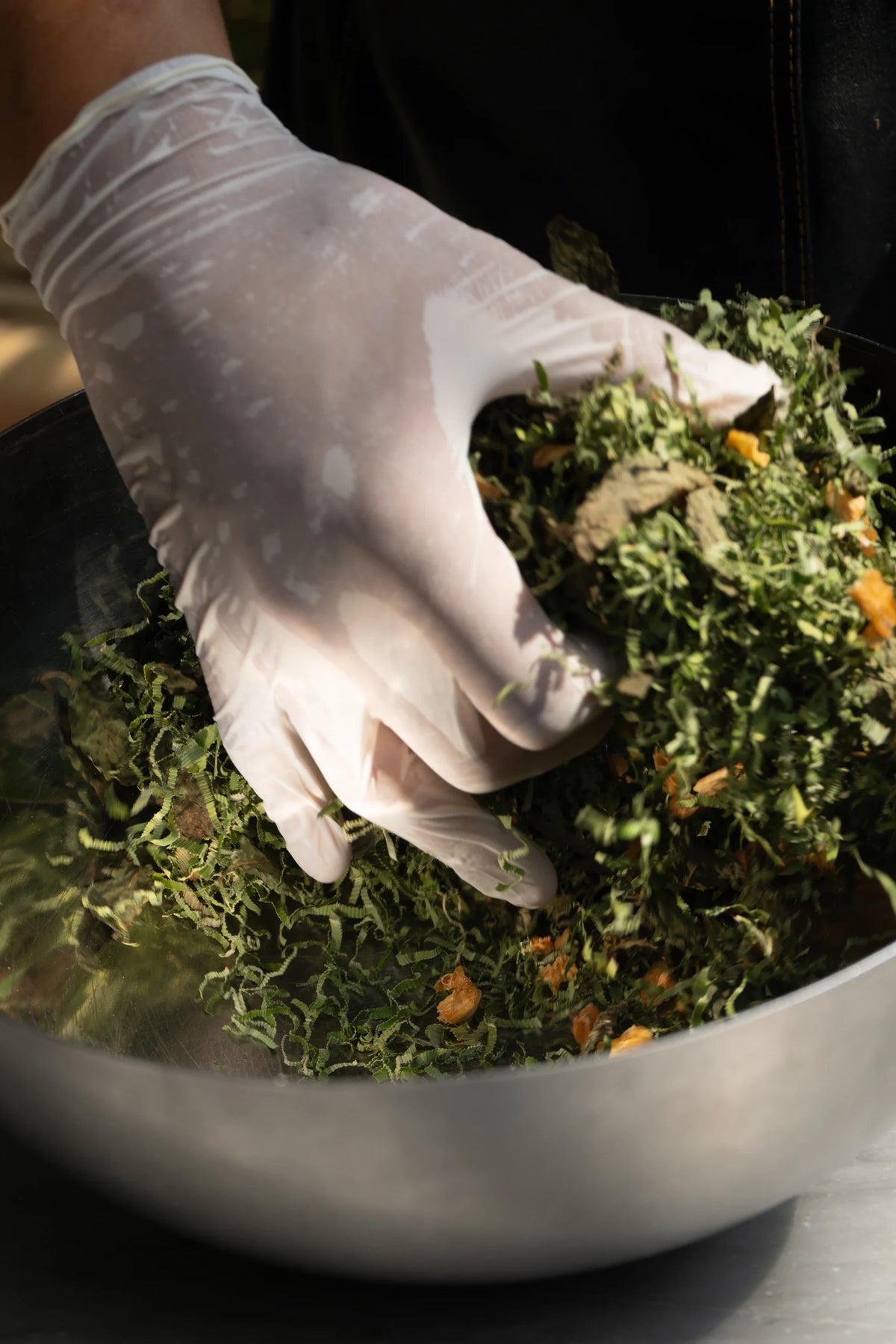 Hand wearing a white glove handling green leafy vegetables in a bowl