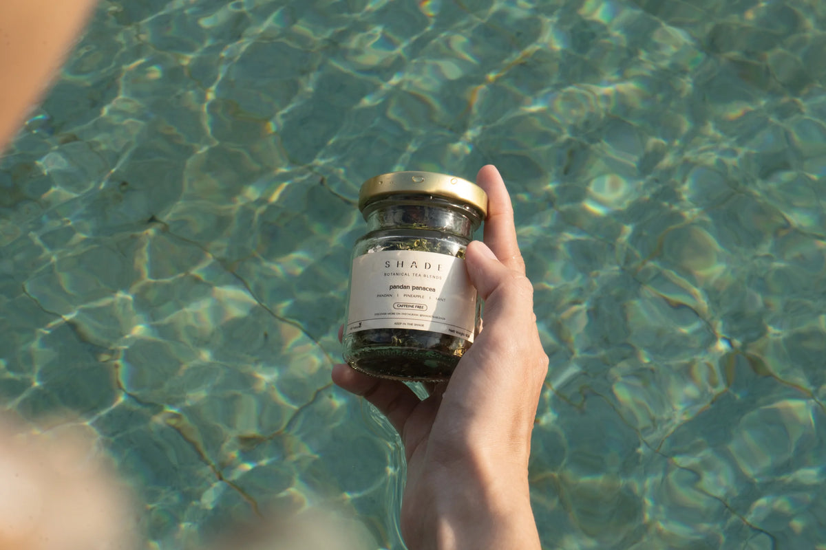 Hand holding a jar of Shade Botanicals Tea Blend with a pool in the background