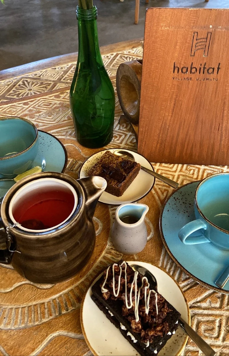 Tea set with brown teapot, blue cups, and pastries on a patterned tablecloth with 'habitat' branding