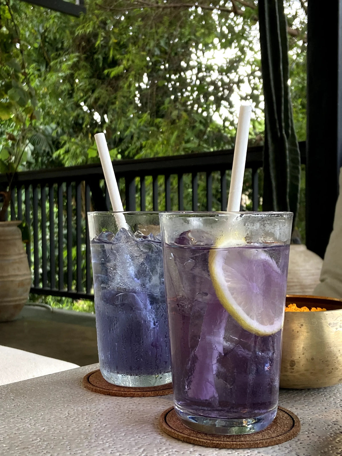 Two glasses of purple iced drinks with lemon slices and straws on a table outdoors