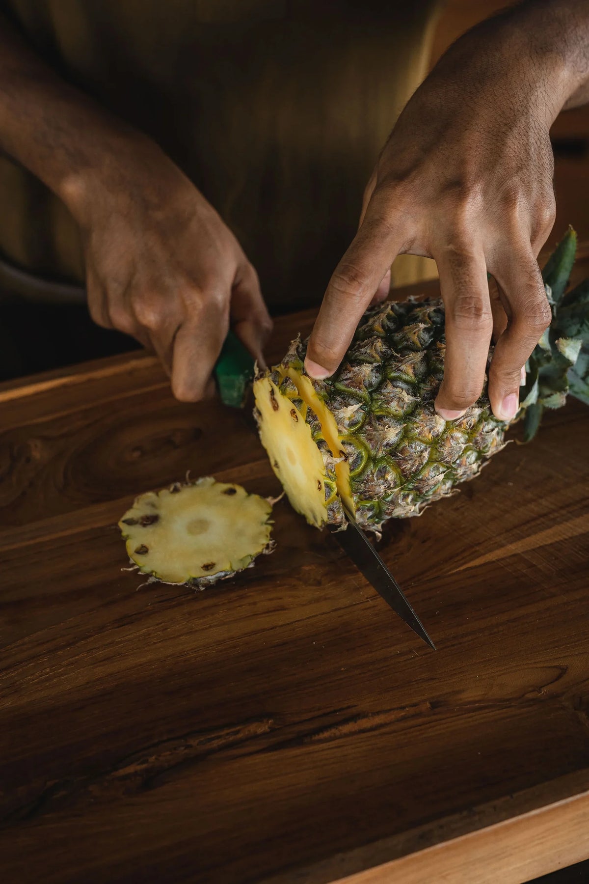 Person cutting a pineapple on a wooden surface
