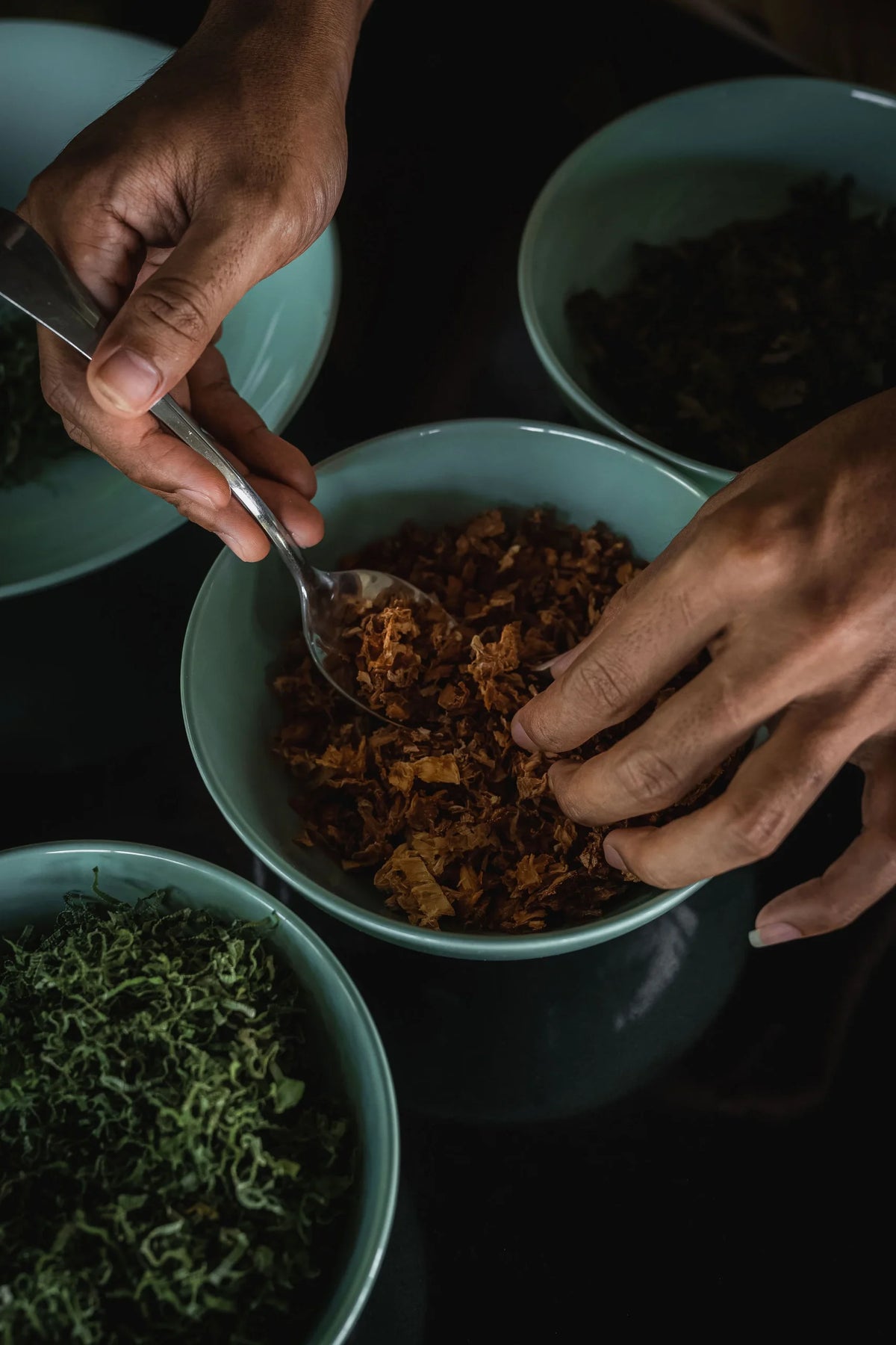 Hands scooping food from a bowl with other bowls of food on a dark surface