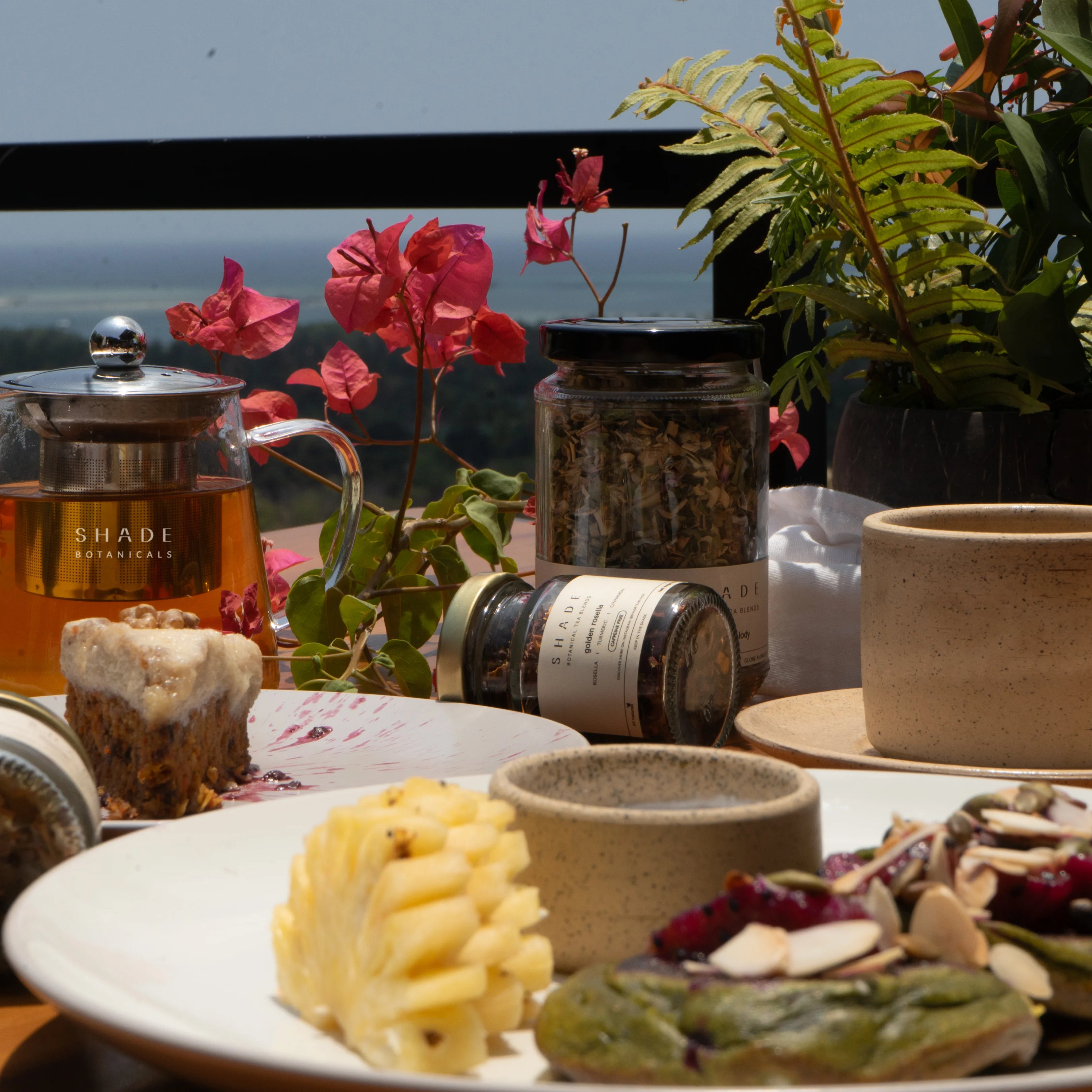 Table with Shade Botanicals Tea Blend, snacks, and plants with a scenic background
